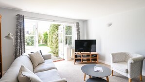 A living room with a sofa, armchair, and a TV on a stand. - 12 The Gardens (Lyme Regis)