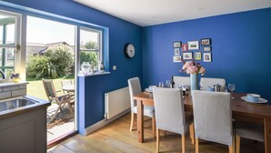 A dining room with a table set for four, a white radiator, and a window with a view of the garden. - 12 The Gardens (Lyme Regis)