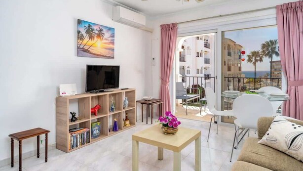 A living room with a TV, bookshelf, and a table with flowers.