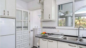 A kitchen with white cabinets, a black countertop, a sink, and a window with a view of palm trees.