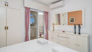 A hotel room with a bed, a dresser, a mirror, and a balcony with pink curtains.