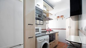 A compact kitchen with a washing machine, microwave, and a small dining area. - Apartment 'Casa Milagros' close to the Sea with Balcony (Sanlúcar de Barrameda)