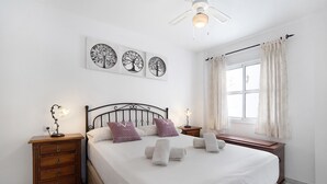 A neatly arranged bedroom with a bed, bedside tables, wall art, and a window with curtains. - Apartment 'Casa Milagros' close to the Sea with Balcony (Sanlúcar de Barrameda)