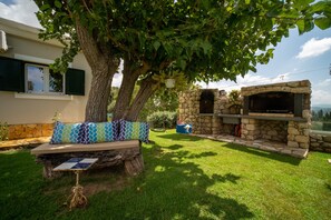 A stone fireplace, a bench with patterned cushions, and a tree in a backyard.