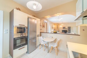 A modern kitchen with a refrigerator, oven, microwave, and dining area with chairs.