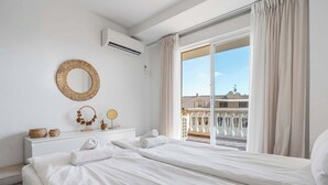 A hotel room with a bed, a dresser, a mirror, and a view of a balcony with buildings.