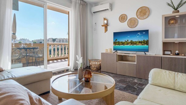 A modern living room with a large TV, a balcony with outdoor seating, and a view of the city.