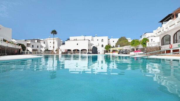 Una piscina con edificios blancos al fondo.