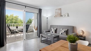 Una sala de estar moderna con un sofá, una mesa de centro, una planta en maceta, una lámpara y un balcón con mobiliario de exterior.
