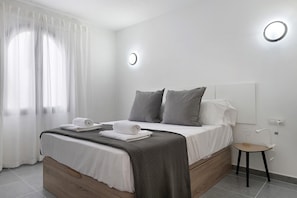 Ein ordentlich bezogenes Bett mit einer karierten Decke, ein Nachttisch mit Lampe und eine Wandleuchte.