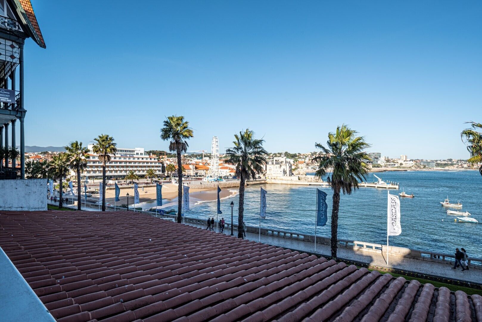 A coastal view with a tiled terrace, palm trees, a beach, and a lighthouse.