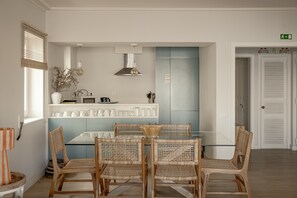 A dining area with a glass table and wicker chairs, a kitchen with white cabinets, and a blue wall.