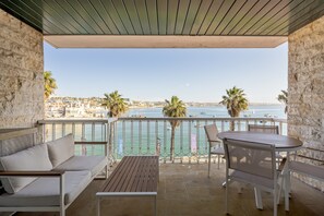 Ein Balkon mit Blick auf das Meer, eine Couch, ein Tisch und Stühle.