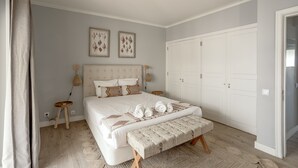 Une chambre à coucher comprenant un lit, des tables de chevet, un banc, une armoire et des œuvres d’art accrochées au mur.