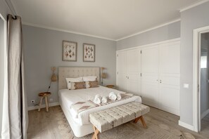 Une chambre à coucher comprenant un lit, des tables de chevet, un banc, une armoire et des œuvres d’art accrochées au mur.