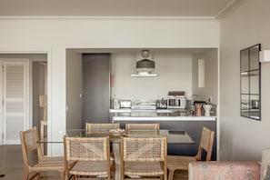 Une cuisine moderne avec un coin repas, comprenant des chaises en osier, une table en verre et un îlot central doté d’appareils de cuisine.