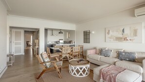 Un salon avec un canapé, des fauteuils, une table basse et, au fond, une cuisine.