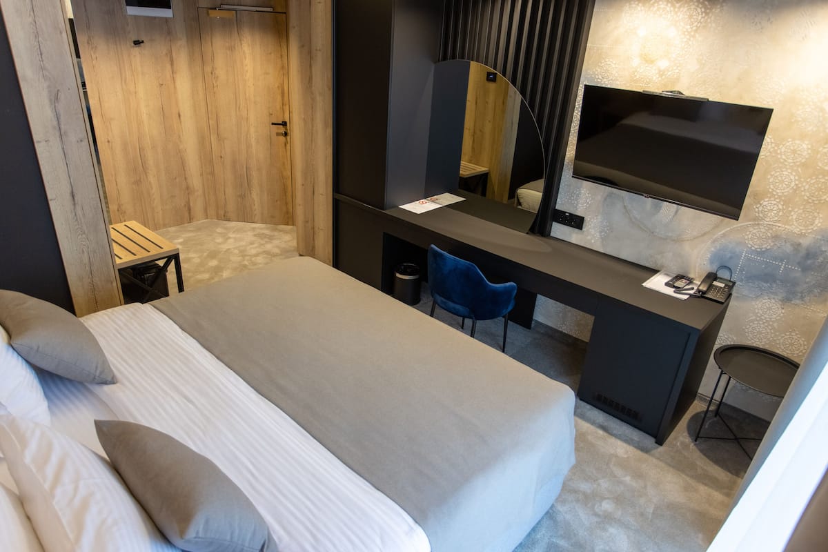 A modern hotel room with a bed, desk, chair, and a flat-screen TV mounted on the wall.