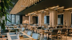 Een modern restaurant met meerdere eettafels en stoelen, houten details en grote ramen.