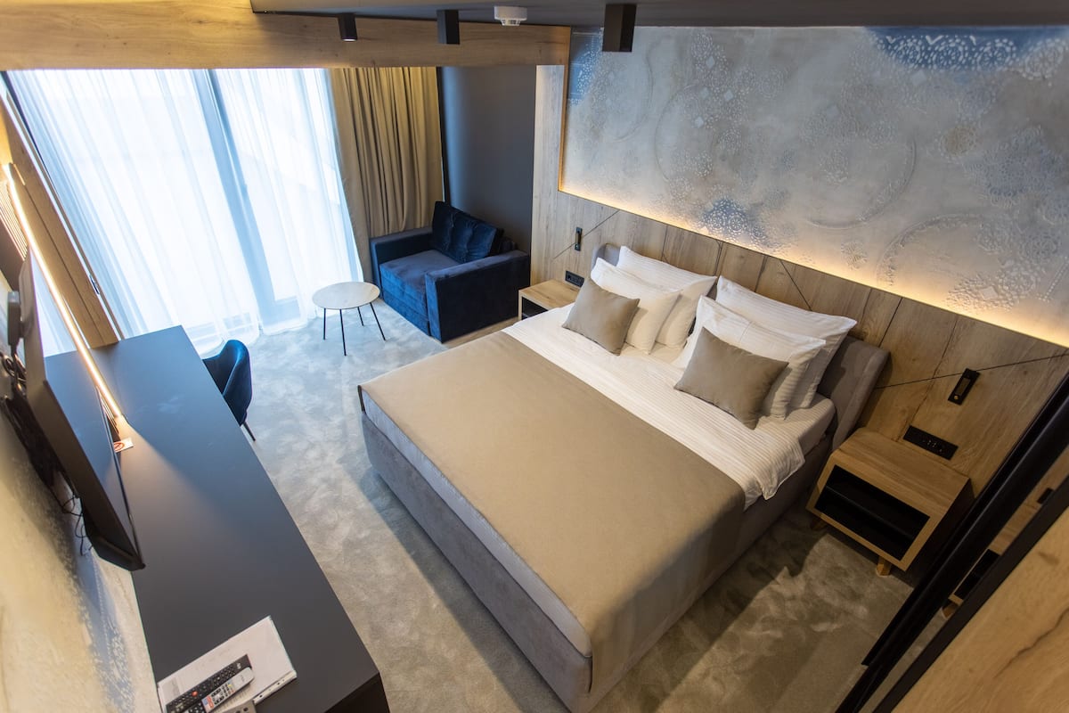A modern hotel room with a large bed, a desk, a chair, and a small table.