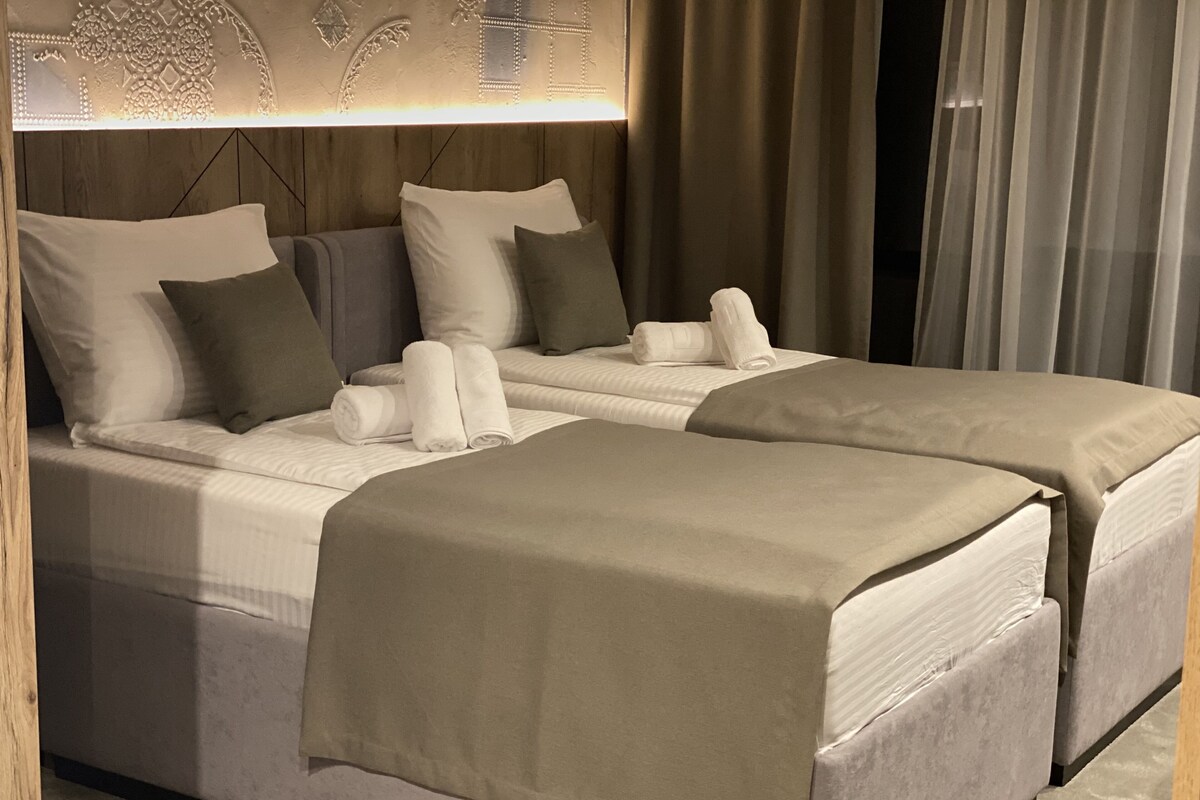 A hotel room with two beds, a wooden headboard, and a decorative wall panel.