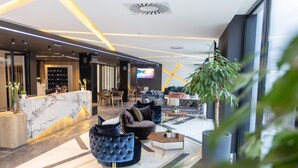 Een moderne lobby met een receptiebalie, een zithoek en een televisiescherm.