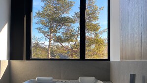 Een moderne badkamer met een groot bad vol bubbels, een raam met uitzicht op bomen, en een minimalistisch ontwerp.