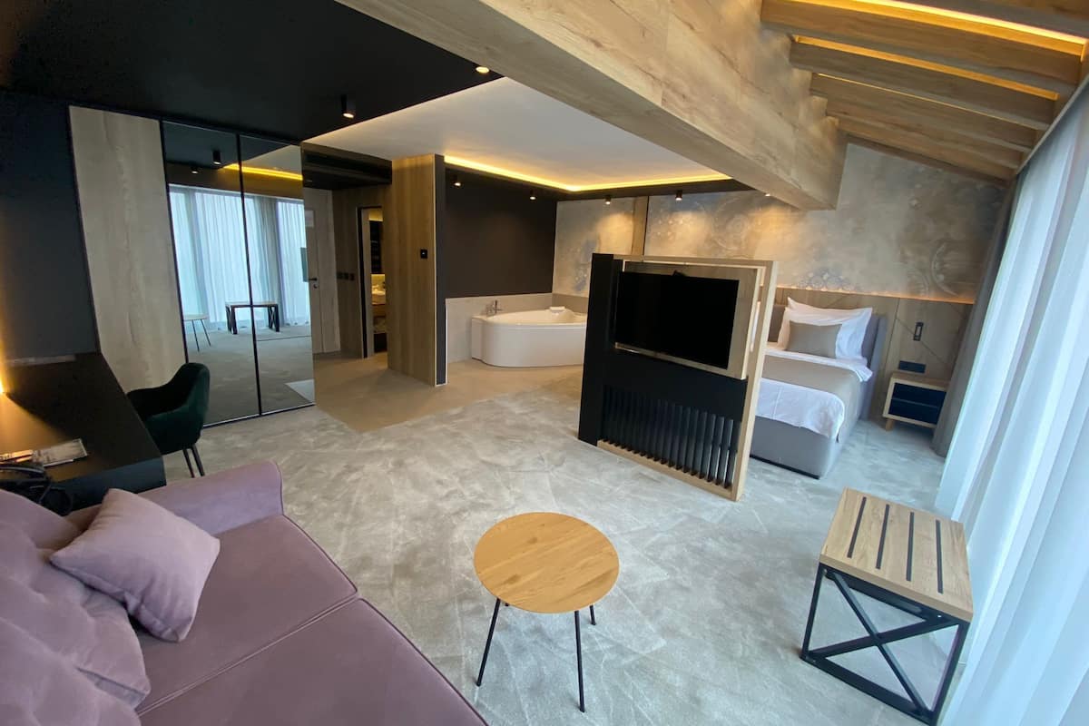 A modern hotel room with a large bed, a TV, a sofa, and a small table.