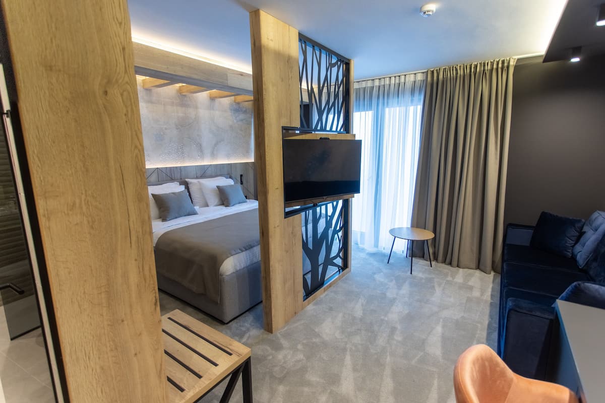 A modern hotel room with a bed, a TV, a seating area, and a view of the outdoors.