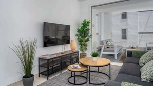 Un salon moderne avec un canapé, une table basse et un téléviseur. On y trouve une plante en pot et une petite table d’appoint avec une lampe.
