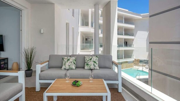 Un appartement moderne doté d’un balcon, d’un canapé avec des coussins, d’une table basse et offrant une vue sur une piscine.