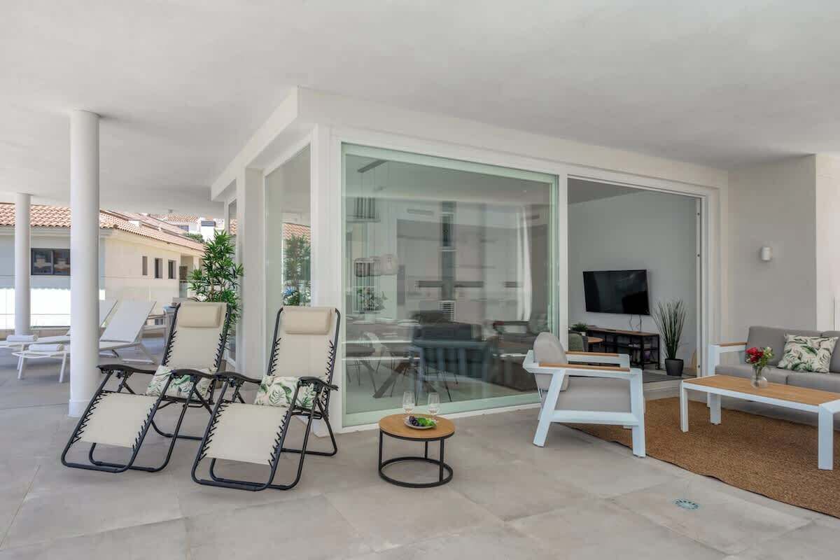 A modern living area with a glass sliding door leading to a balcony, furnished with lounge chairs and a coffee table.