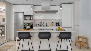 Une cuisine moderne avec des armoires blanches, une hotte de cuisinière en acier inoxydable et trois tabourets de bar noirs.