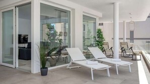 Un balcon intérieur moderne, avec des fauteuils blancs, un coin repas doté de portes vitrées et des plantes en pot.