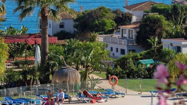Zona de piscina con sillas de descanso, palmeras y vista al océano.