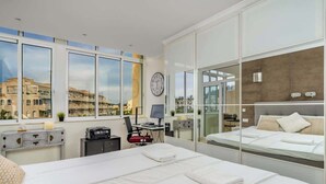 Habitación de hotel moderna con una cama grande, un escritorio y vistas a la ciudad a través de ventanales de suelo a techo.