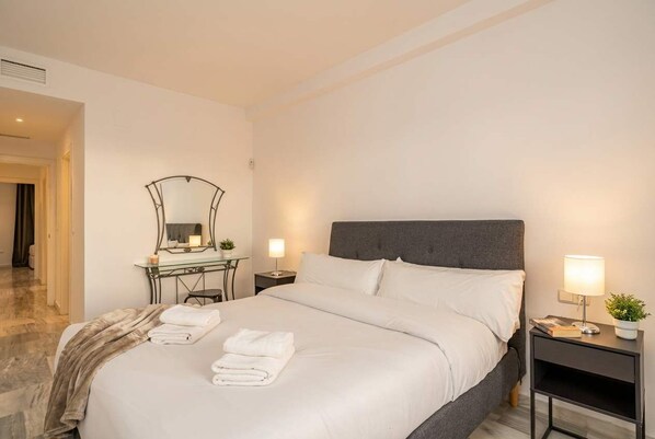 A hotel room with a large bed, bedside tables with lamps, a mirror, and a small plant.
