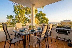 Une terrasse extérieure avec une table dressée pour les repas, des chaises et un barbecue.