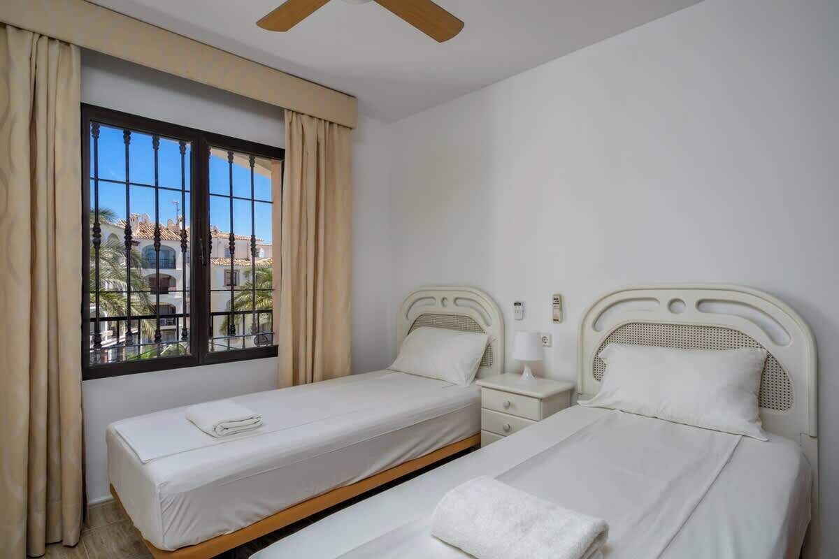 Ein Hotelzimmer mit zwei Betten, einem Fenster mit Vorhängen und einem Deckenventilator.
