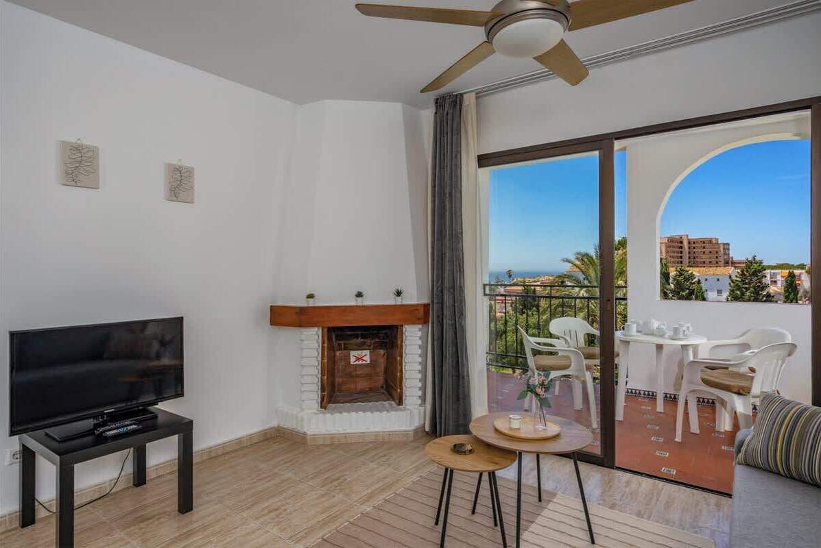 Una sala de estar moderna con una televisión de pantalla plana, chimenea, ventilador de techo y balcón con mobiliario exterior.
