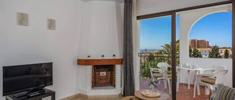 Una sala de estar moderna con una televisión de pantalla plana, chimenea, ventilador de techo y balcón con mobiliario exterior.