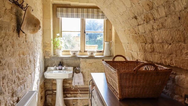 A rustic bathroom with a stone wall, a white pedestal sink, a radiator, and a wicker basket on a wooden counter.
