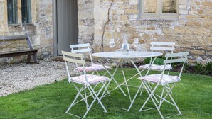 A stone building with a small garden patio featuring a round table, four chairs, and a bench.