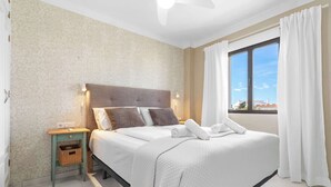 A bedroom with a bed, nightstand, and window with curtains. - Riviera Bright Balcony by Costarentals - Ref 184 (Las Lagunas de Mijas)