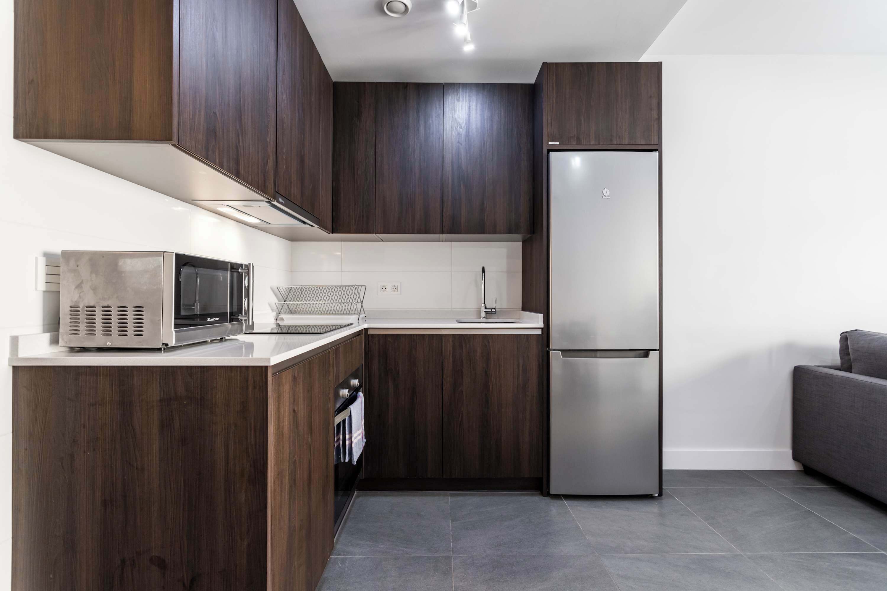 A modern kitchen with dark wood cabinets, stainless steel appliances, and a grey tiled floor.