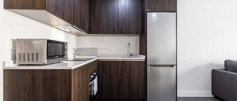 A modern kitchen with dark wood cabinets, stainless steel appliances, and a grey tiled floor.