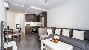 A modern living room with a grey sofa, white coffee table, and a dining area with a table and chairs.