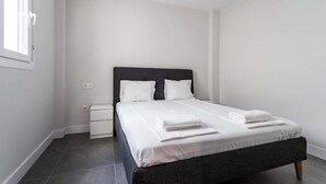 A modern bedroom with a dark headboard, white bedding, and a neatly made bed.