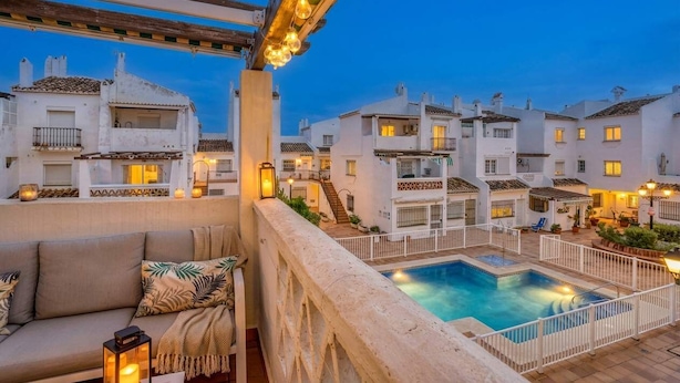 A rooftop pool area with a white pool, a wooden pergola with hanging lights, and white buildings in the background. - Beachfront Apartment w/ Pool & Golf Access - La Duquesa (Málaga)