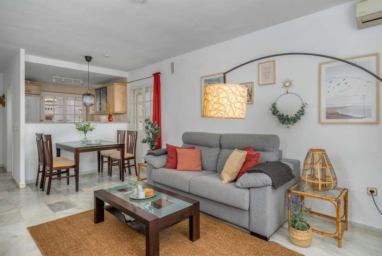 A living room with a grey sofa, wooden chairs, a glass coffee table, and a dining area with a table and chairs.
